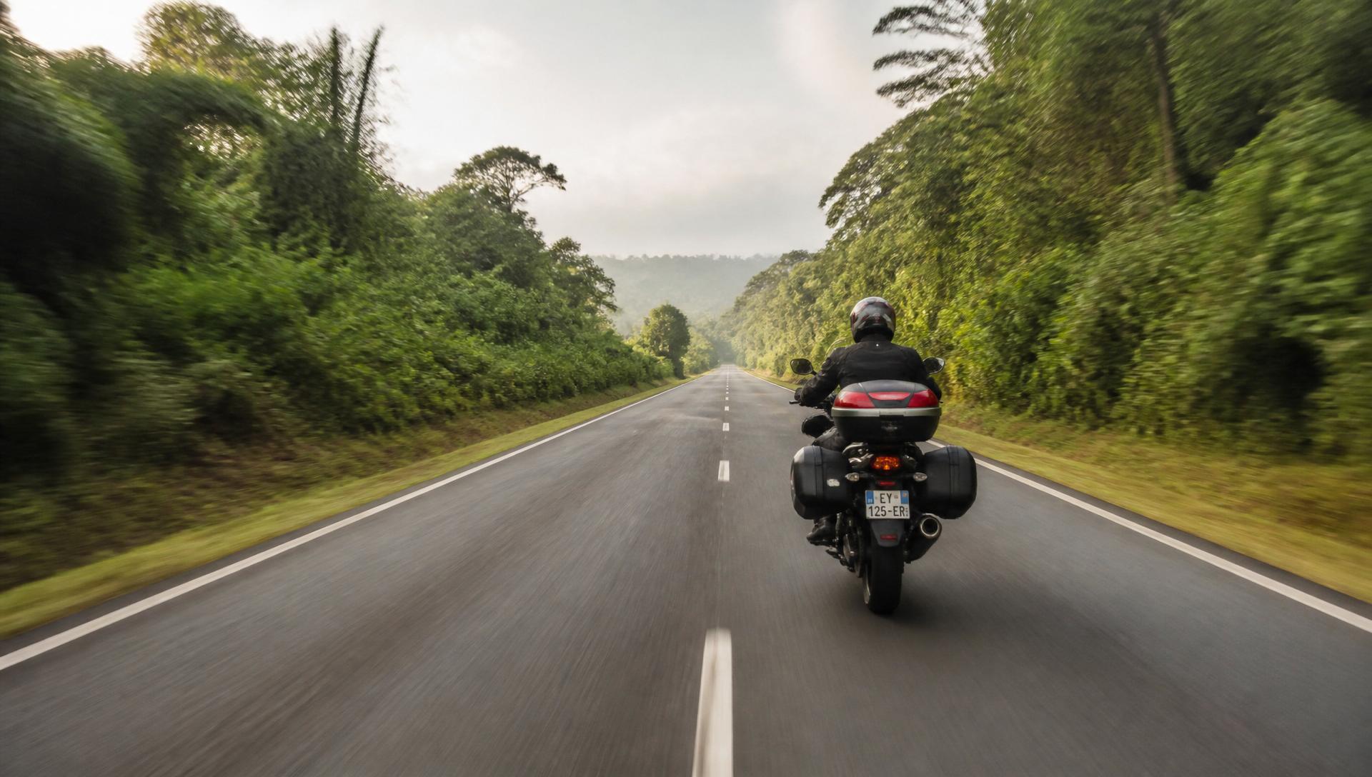 Motard sur une route de Guyane bordée de forêt équatoriale